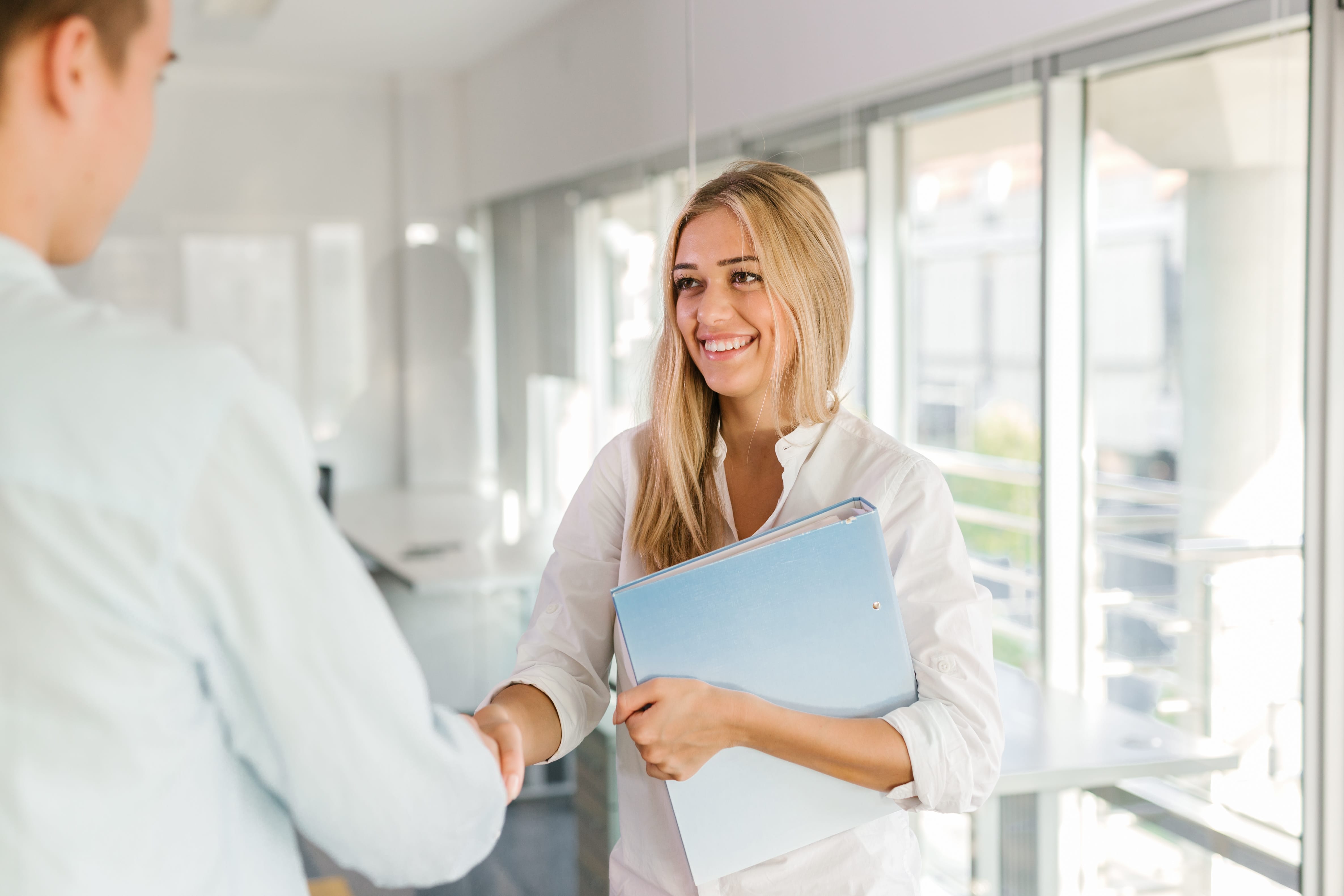 Woman holding a folder smiling while shaking hands.